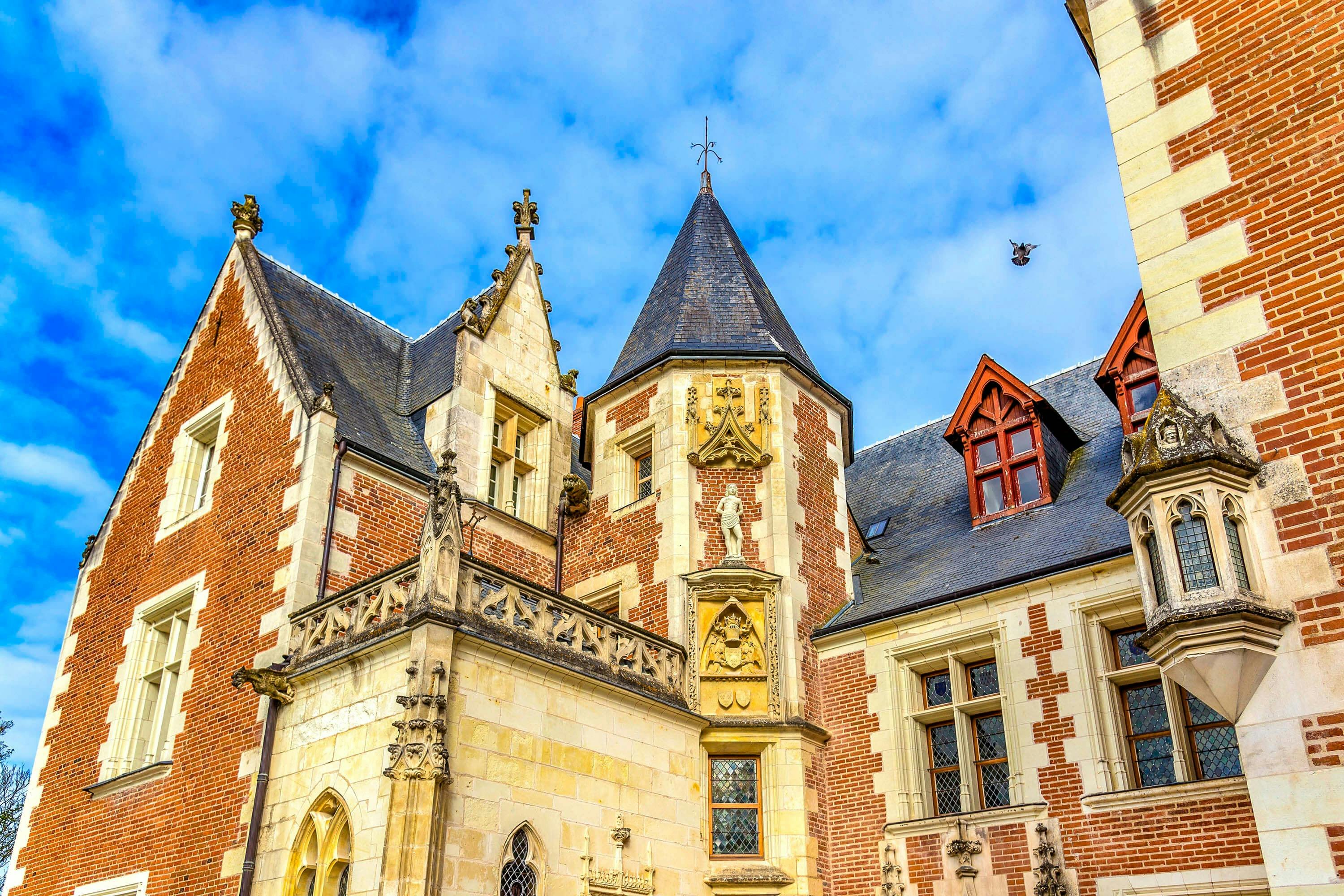 정교한 건축 디테일, 높은 뾰족한 지붕, 푸른 하늘을 배경으로 한 유서 깊은 벽돌과 석조 건물.