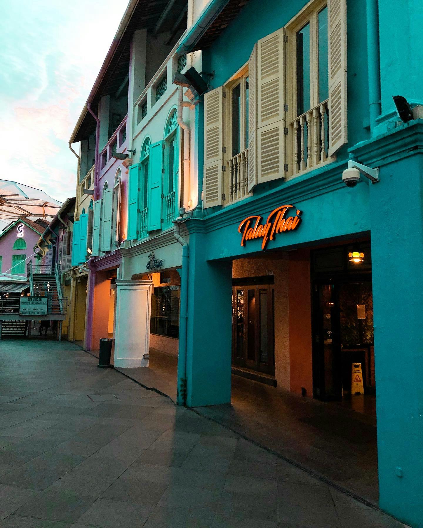 Edifici colorati con persiane fiancheggiano una strada pedonale. Un'insegna visibile recita "Talay Thai".