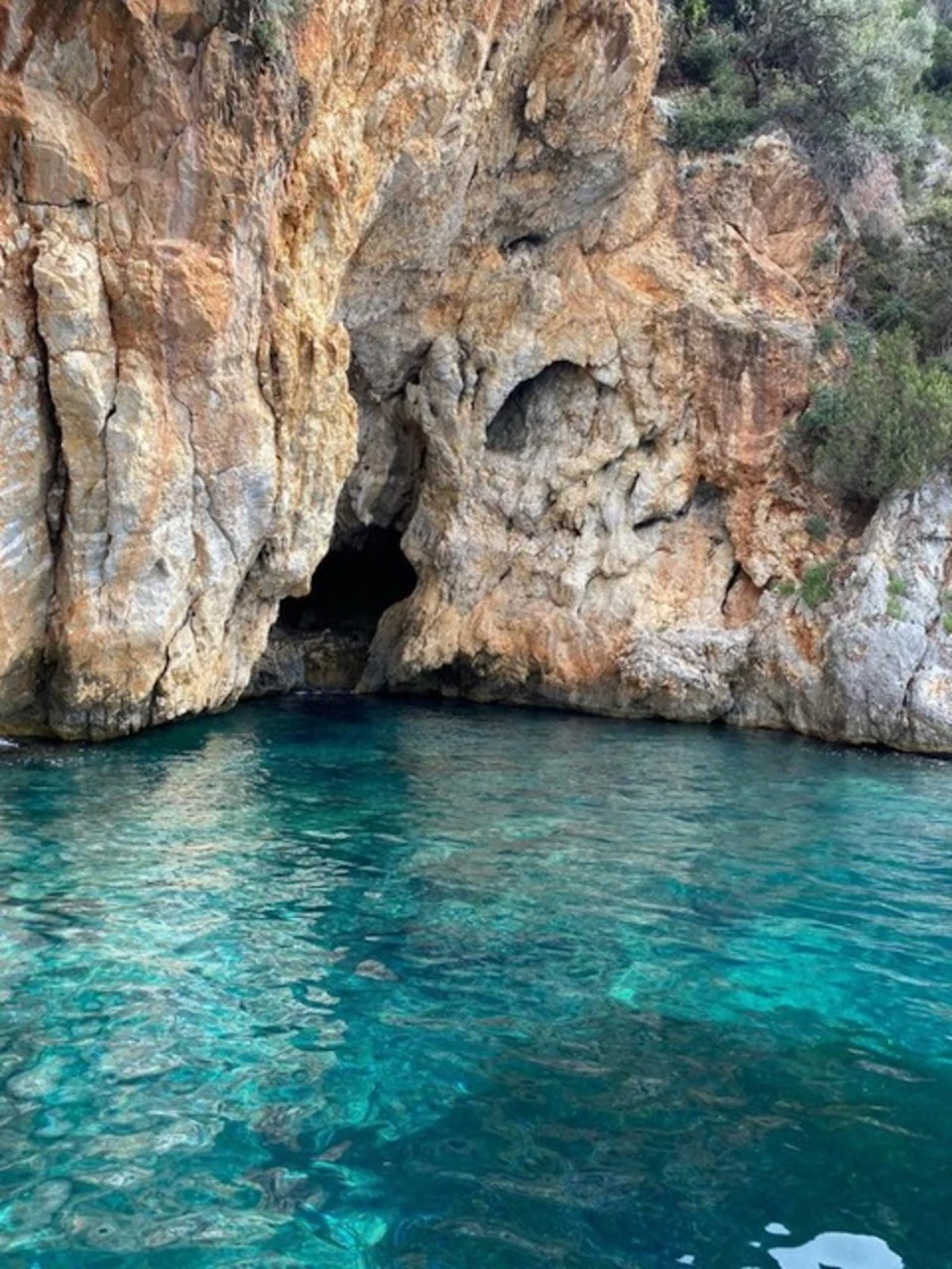 Clear turquoise water in front of a rocky cliff with a dark cave entrance.