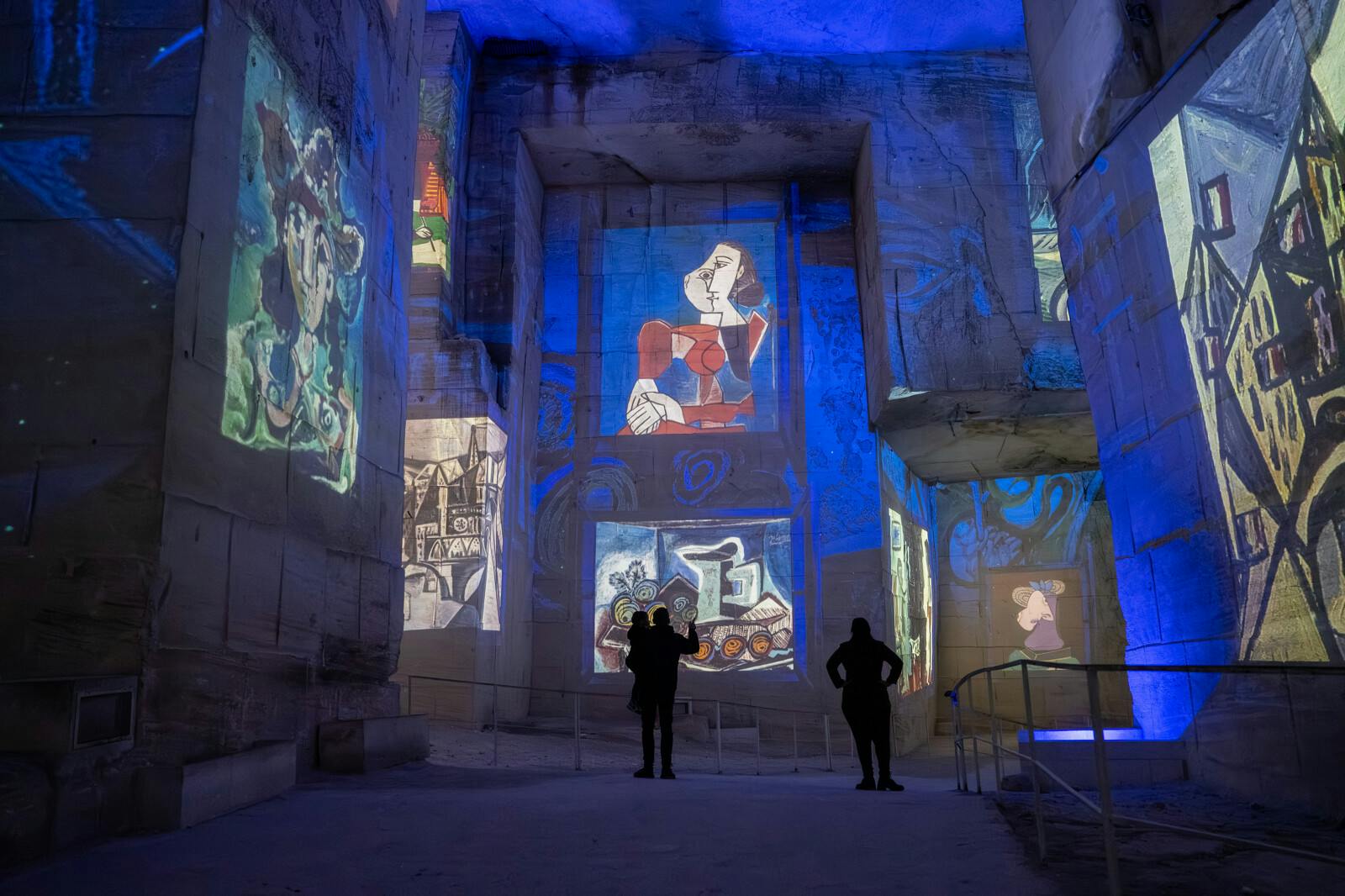 Two people silhouetted against walls of a cavernous space illuminated by colorful projected art and blue lighting.