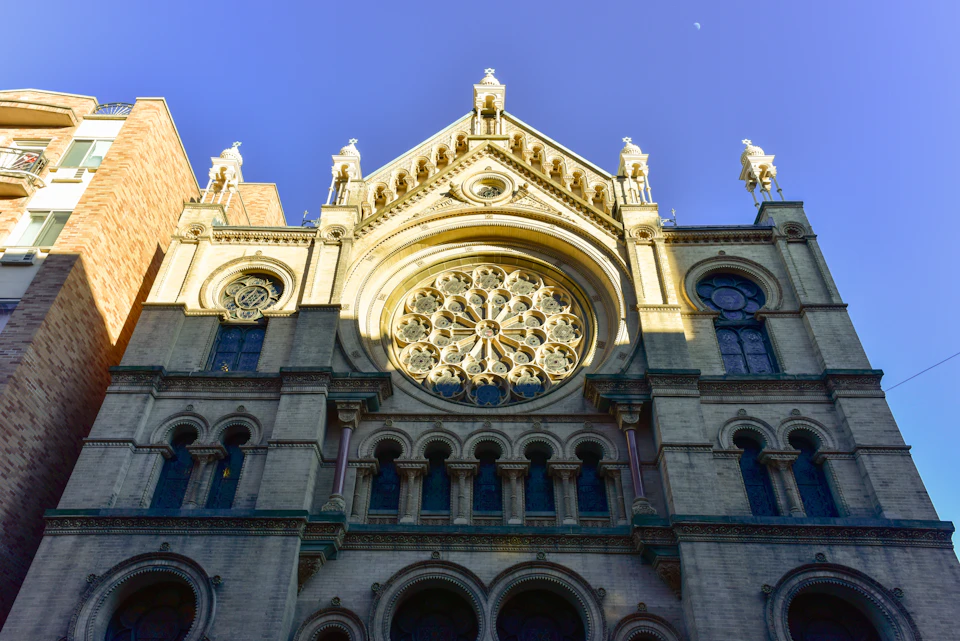 Facade of a gothic-style building with a large circular stained glass window and intricate architectural details against a clear blue sky.