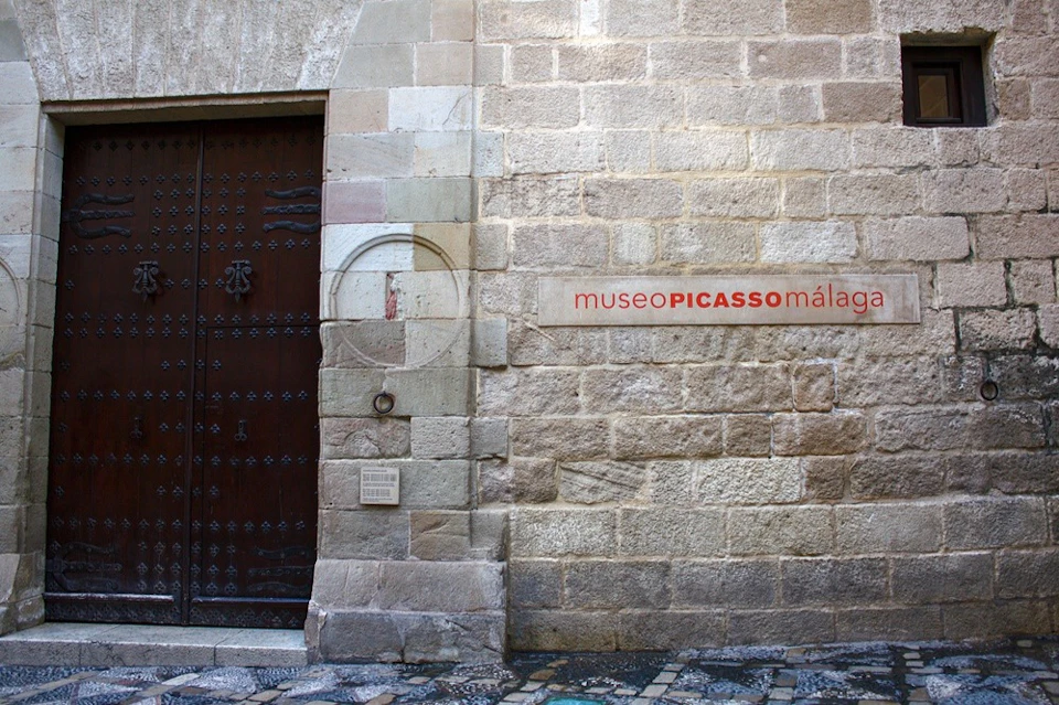 A stone wall with a wooden door and a sign reading "museo PICASSO málaga."