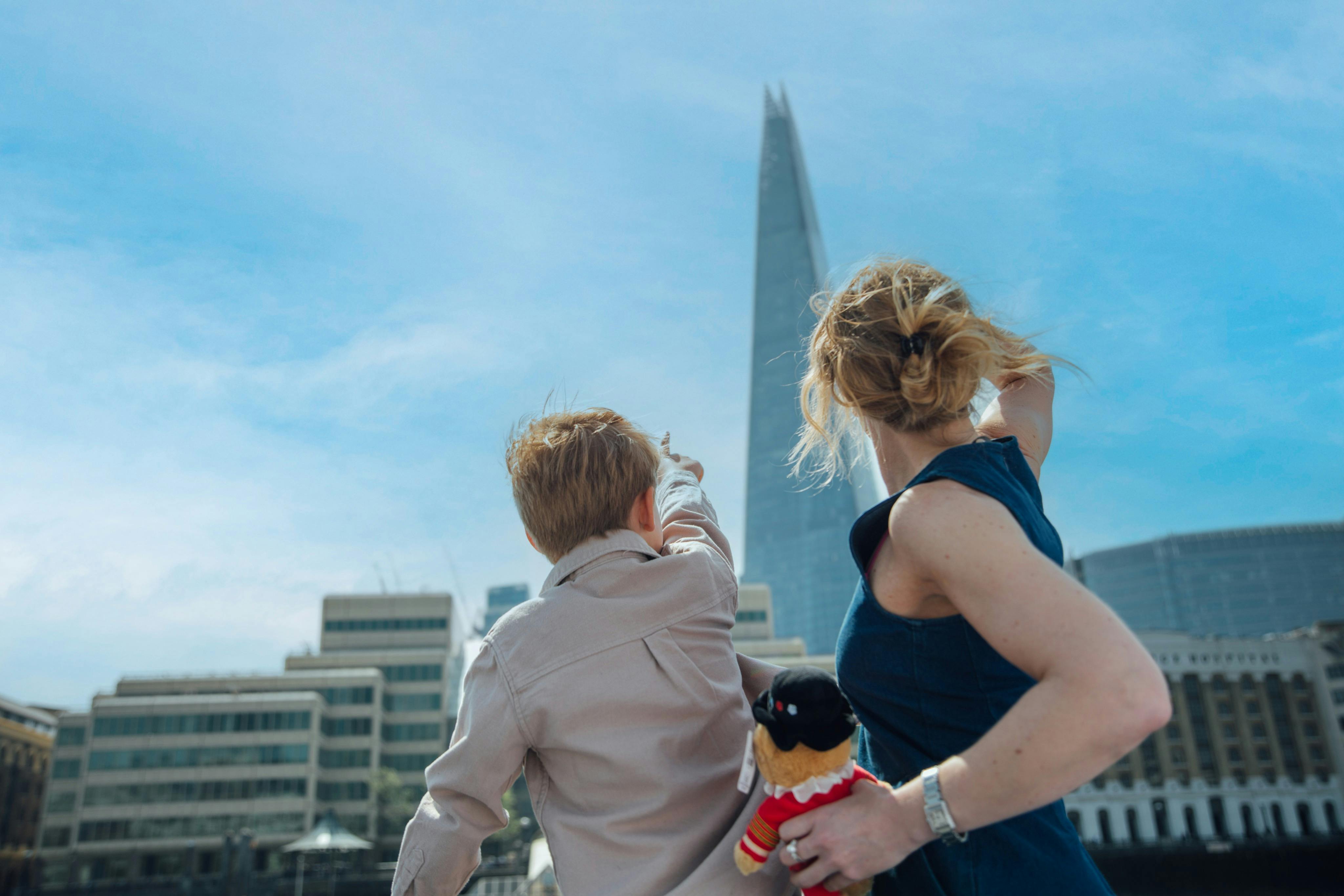 Une femme et un enfant pointant du doigt le gratte-ciel Shard à Londres, avec le paysage urbain et un ciel bleu clair en arrière-plan.