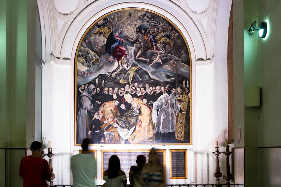 People observing a large, detailed mural depicting a religious scene with numerous figures, in a well-lit, arched gallery space.