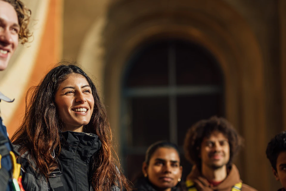 A group of people wearing harnesses posing outdoors near a building with an arched window in the background.