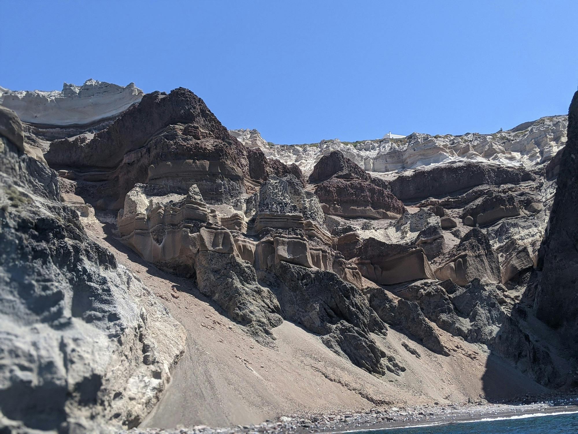 在晴朗的蓝天下，棕色和米色阴影层层侵蚀的悬崖，底部有岩石地形。
