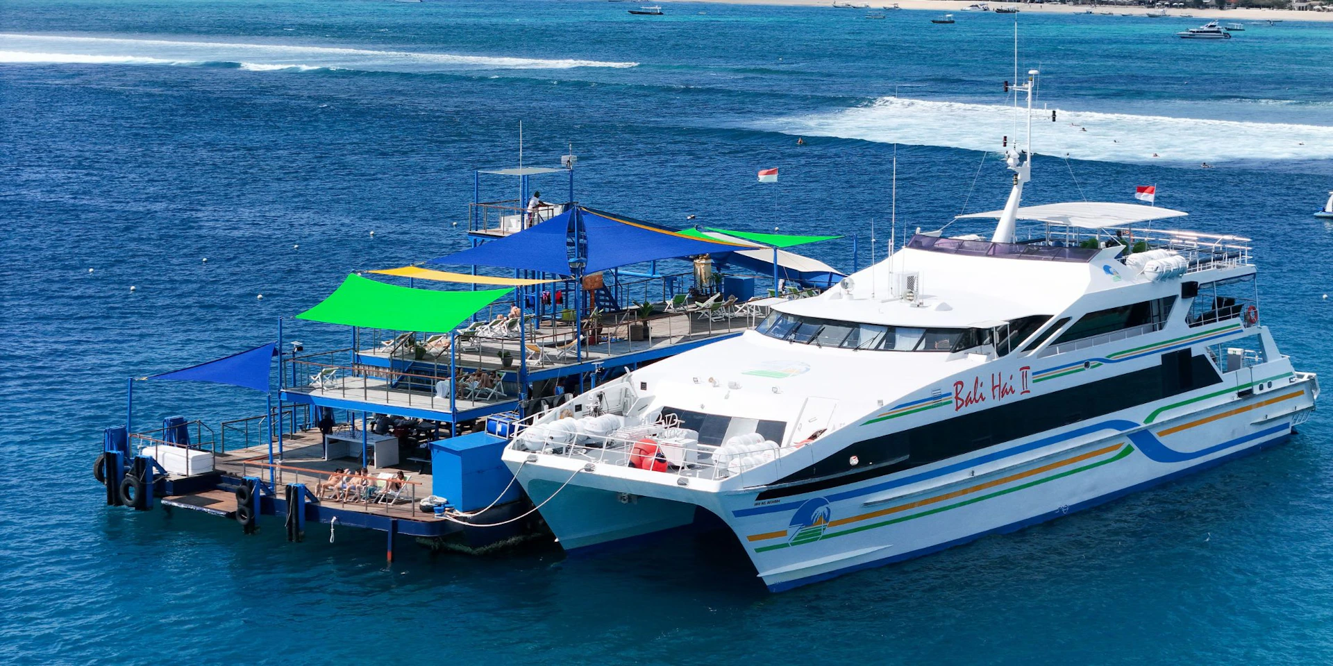 A large catamaran labeled "Bali Hai" docked at a floating platform with green and blue canopies on a clear, sunny day.