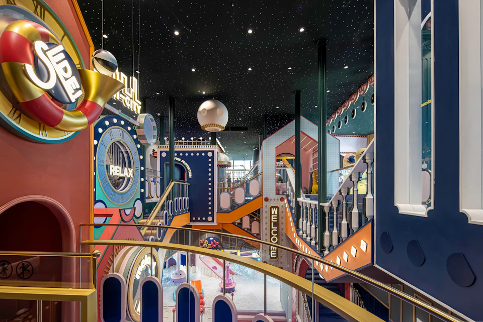 A colorful, futuristic indoor play area with themed decor, stairs, and signs under a starry ceiling.