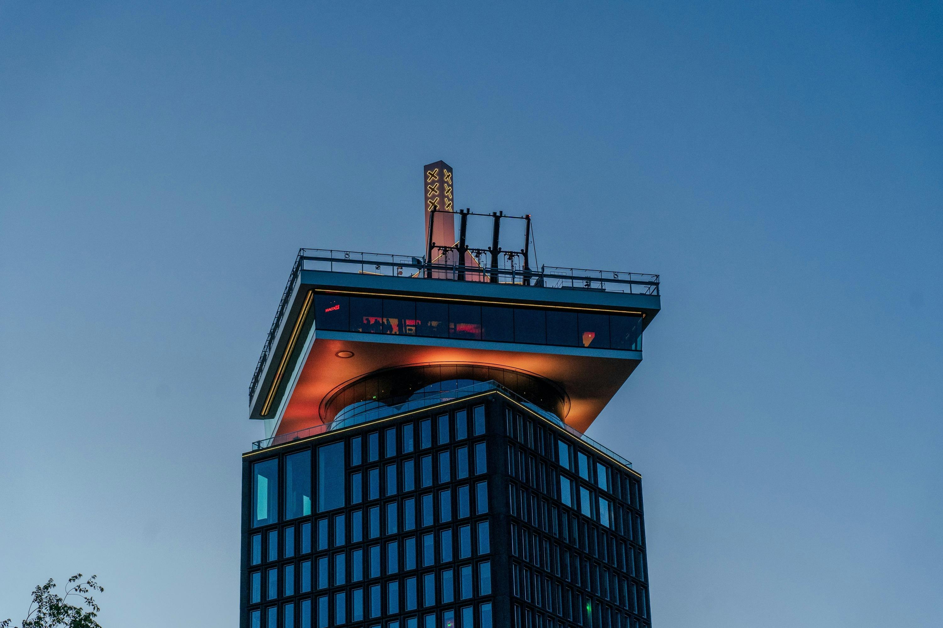 옥상 전망대가 있는 현대적인 고층 건물로 맑은 저녁 하늘을 배경으로 조명이 켜져 있습니다.