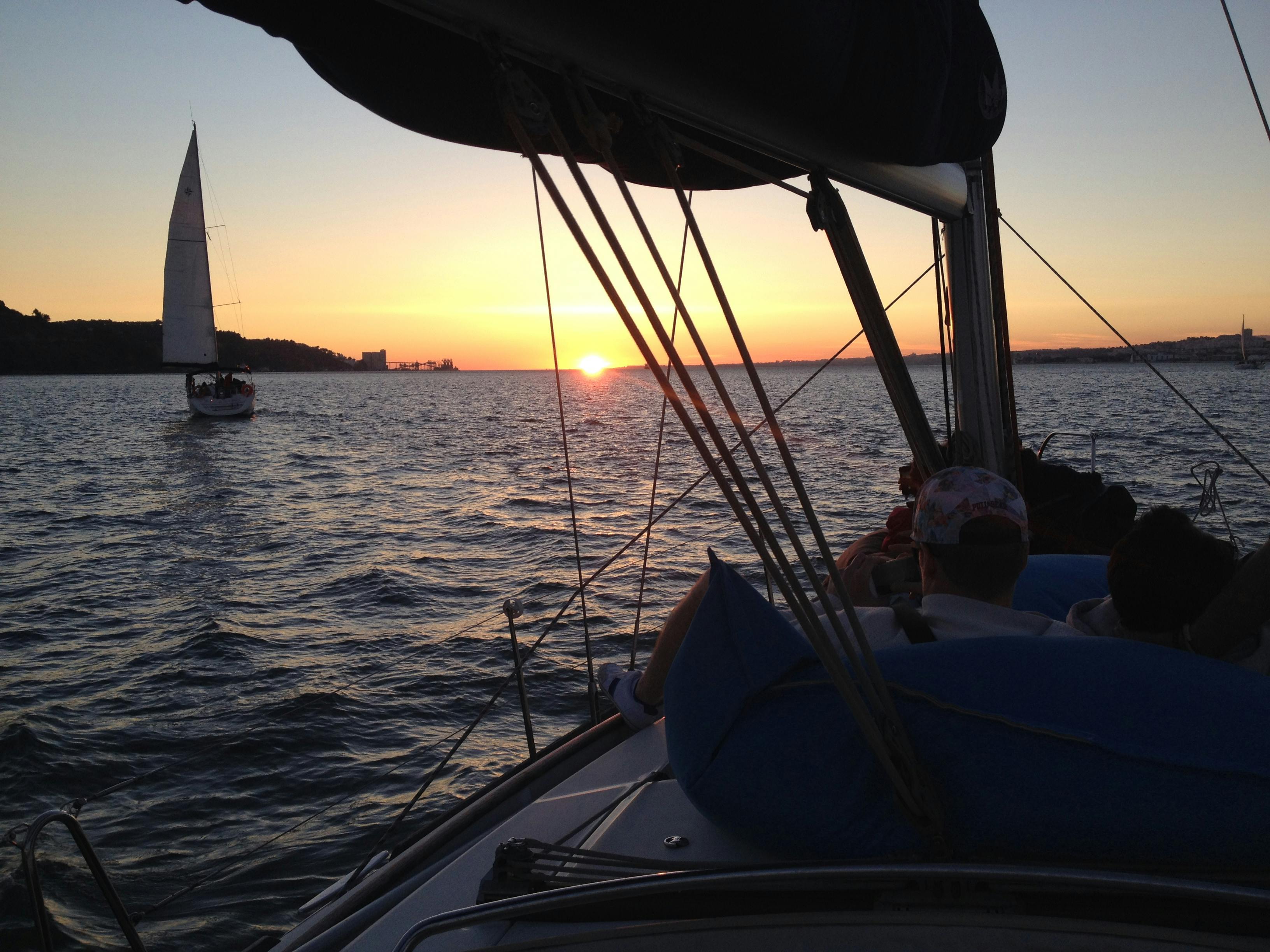 夕暮れ時に帆船に乗っている人々と、遠くの穏やかな海の上に見える別の帆船。