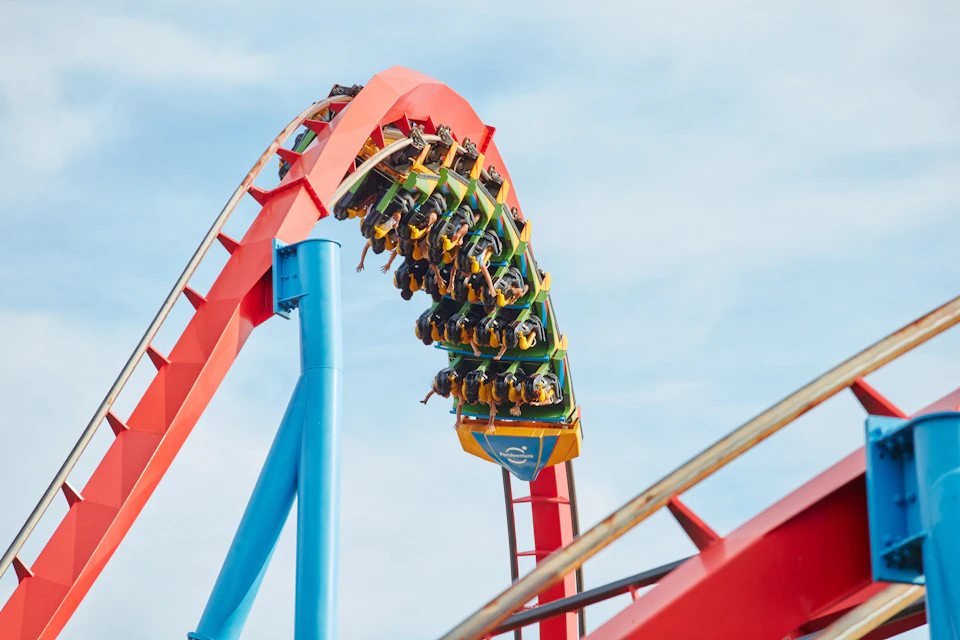 A colorful rollercoaster with passengers upside down on a loop against a blue sky.