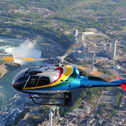 A colorful helicopter flying over a cityscape with tall buildings, a large waterfall, and a Ferris wheel visible below.