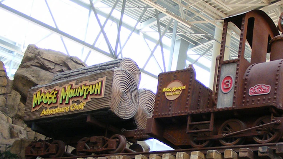 Indoor amusement ride with log-themed decorations and signs that read "Moose Mountain" and "Moose Mountain Shine Road."