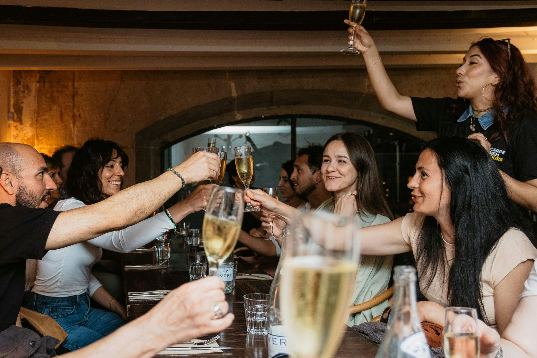Um grupo de pessoas sentadas à volta de uma mesa a baterem copos de champanhe num brinde de celebração.