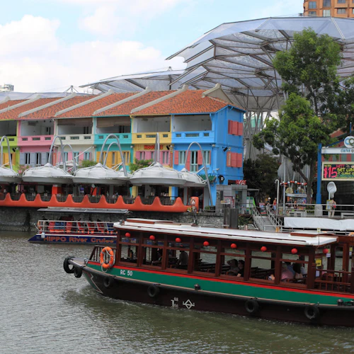 Bunte Gebäude säumen die Uferpromenade am Clarke Quay, Singapur, mit Bootstouren auf dem Fluss davor.