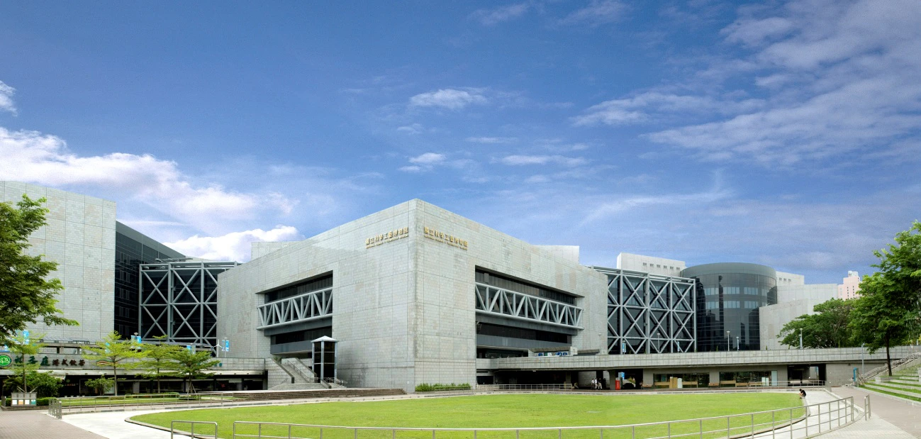 A modern building with a geometric facade, spacious lawn in front, and a clear blue sky in the background.
