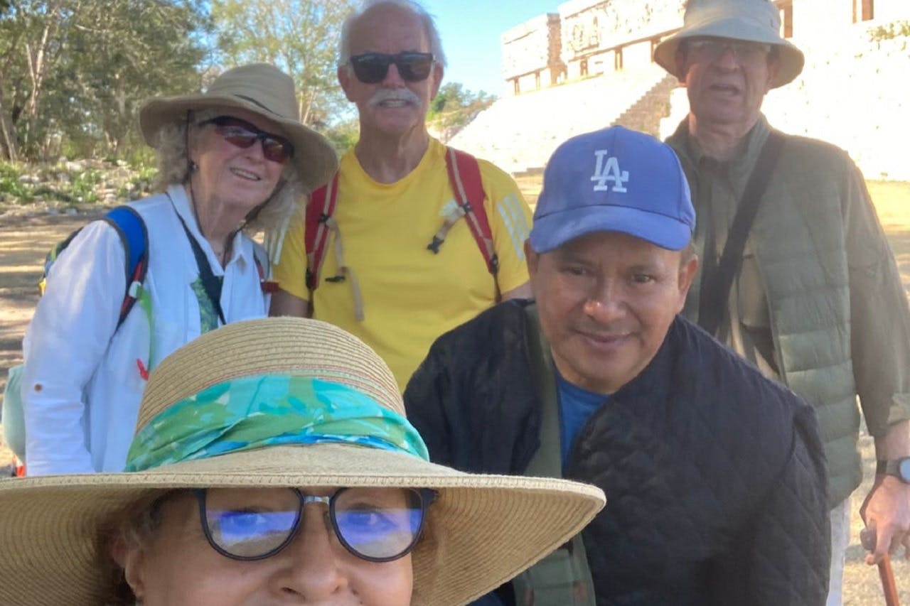 Un groupe de cinq personnes portant des chapeaux sourit à l'appareil photo, avec une ancienne structure en pierre à l'arrière-plan.