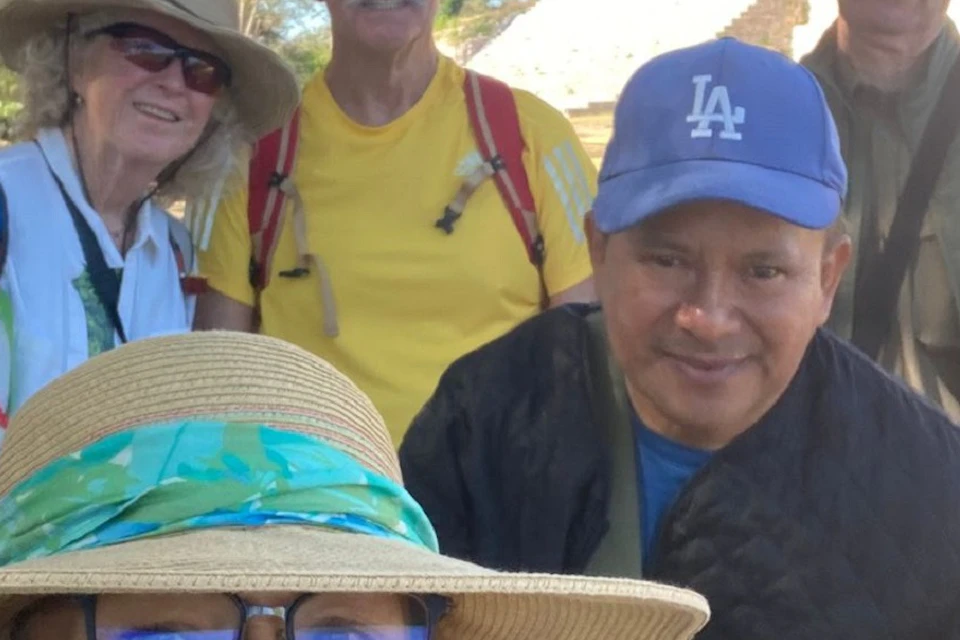 A group of five people wearing hats smile at the camera with an ancient stone structure in the background.