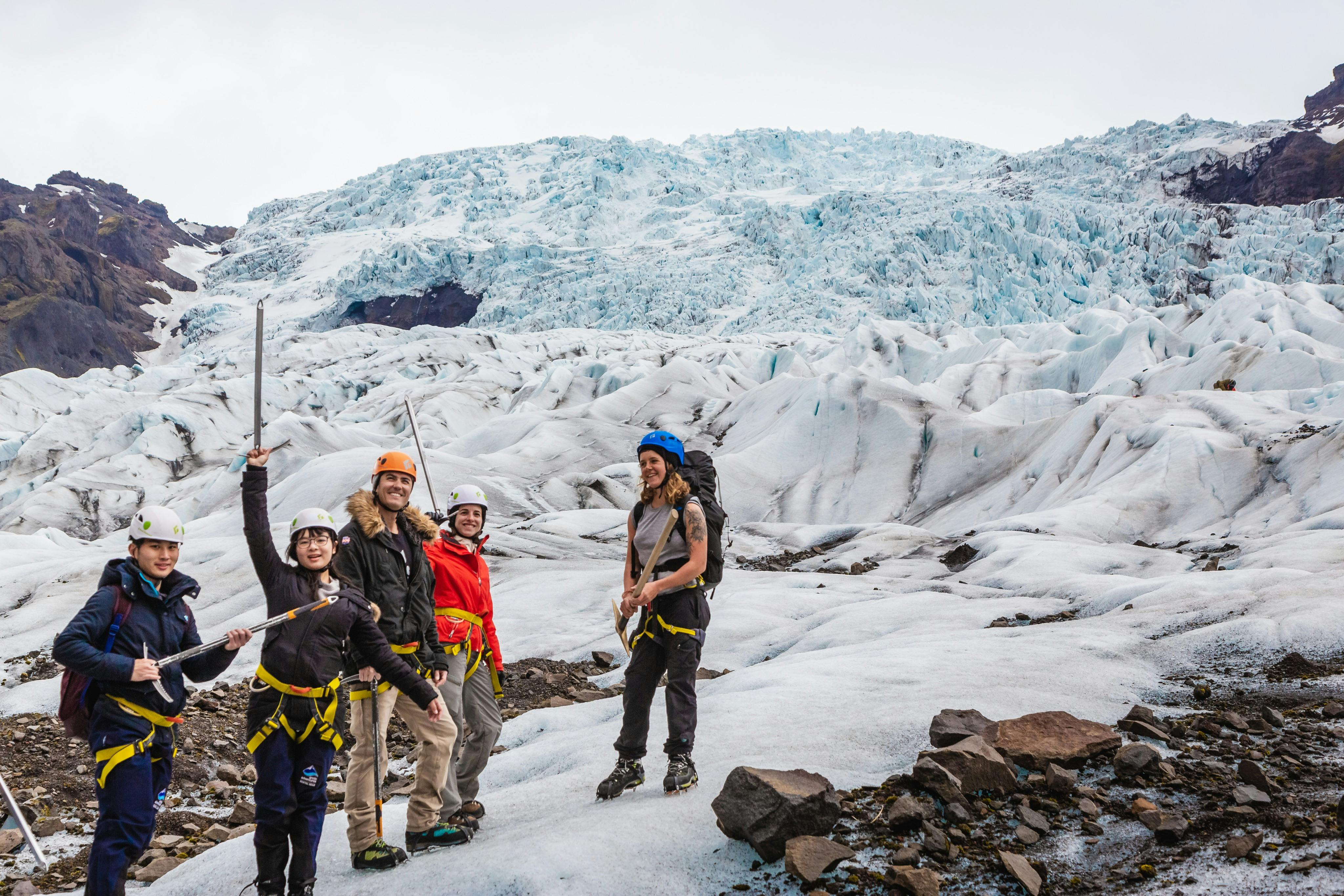 빙하를 배경으로 헬멧과 야외 장비를 착용한 한 무리의 사람들이 얼음 도끼를 들고 빙하 위에 서 있습니다.