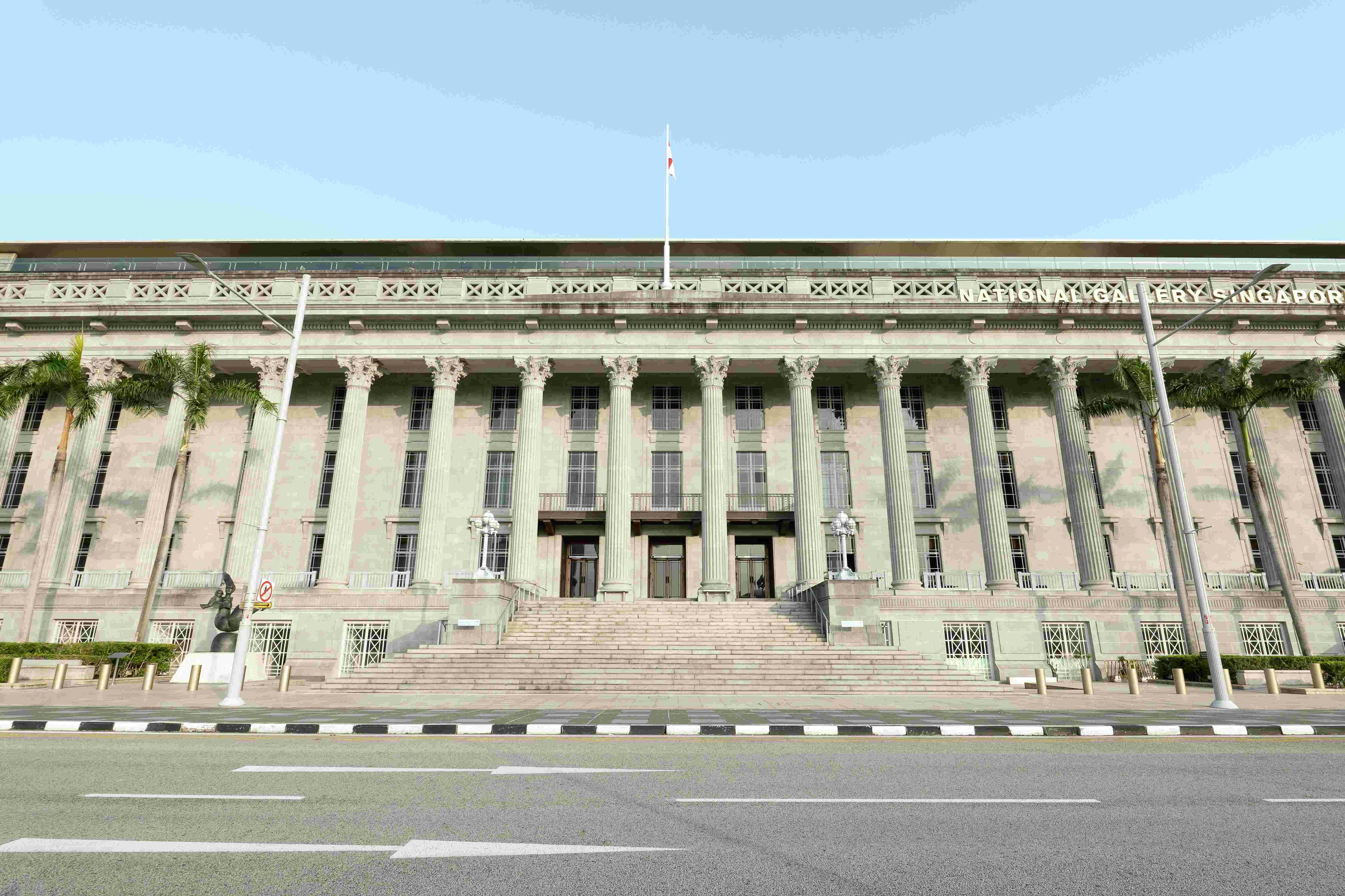 Front facade of a neoclassical building with large columns, stairs leading to entrance, and a flagpole on the roof.