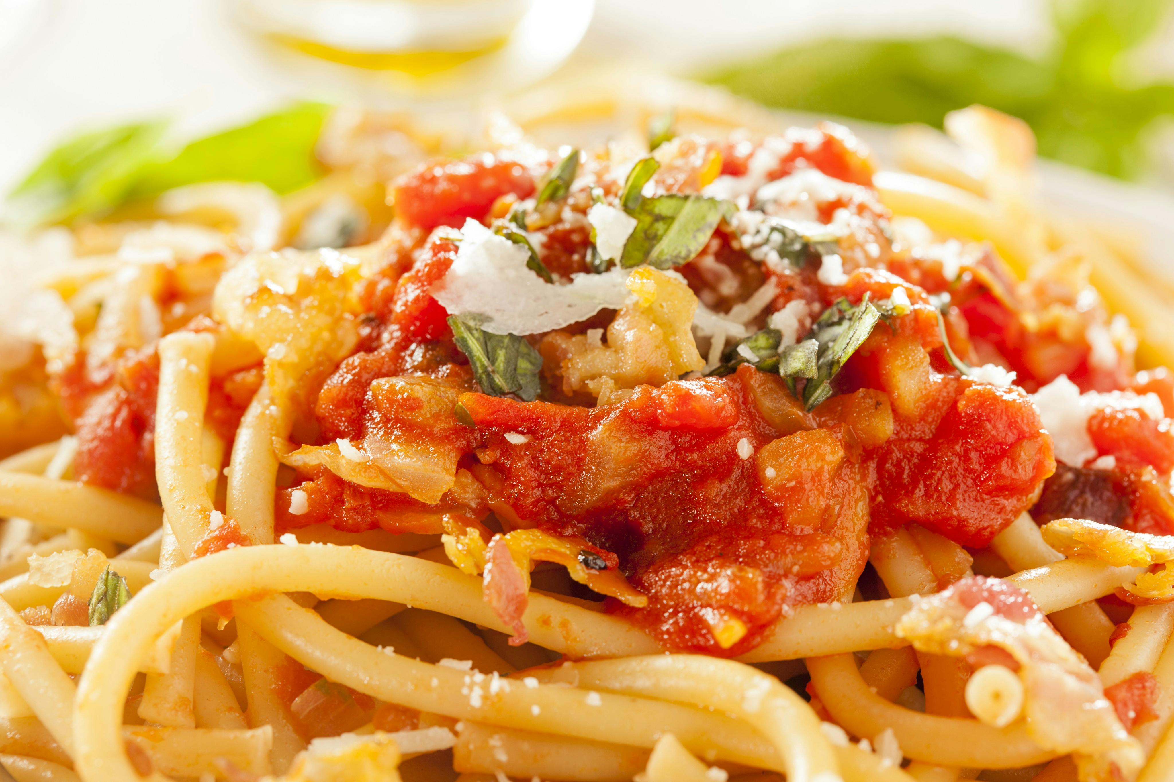 Primo piano di pasta con salsa di pomodoro, formaggio grattugiato e foglie di basilico.