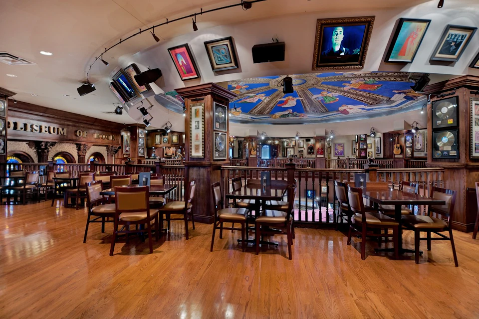 A restaurant interior with wooden floors, tables, and chairs, featuring framed artworks on the walls and ceiling.