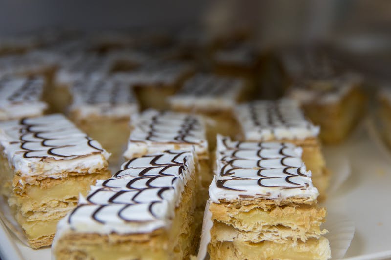 Close-up of layered pastries topped with white icing and chocolate drizzle, arranged in rows on a display.
