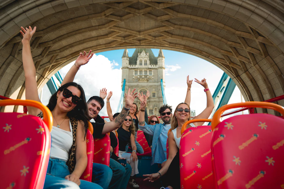 Group of people smiling and posing on a sightseeing bus with a view of Tower Bridge in the background.