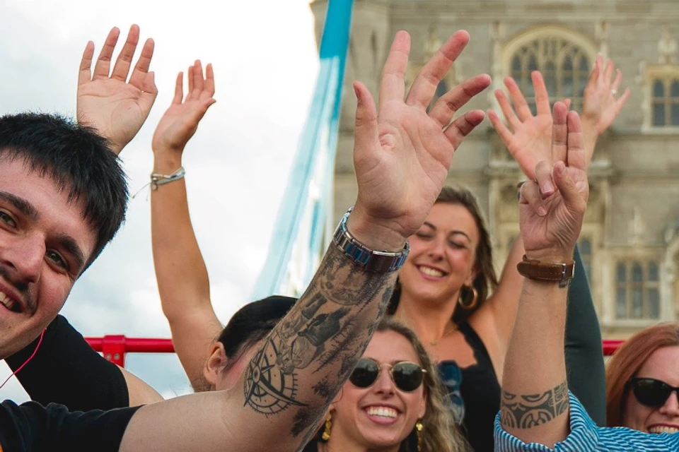 Group of people smiling and posing on a sightseeing bus with a view of Tower Bridge in the background.