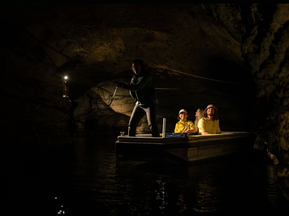 A group of people on a boat inside a dark cave, illuminated by dim lighting.