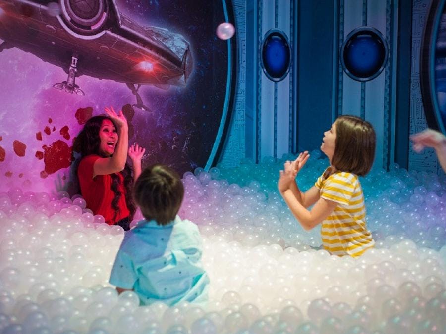 Трое детей играют в яме с космическим фоном, на котором изображен космический корабль и звезды.
