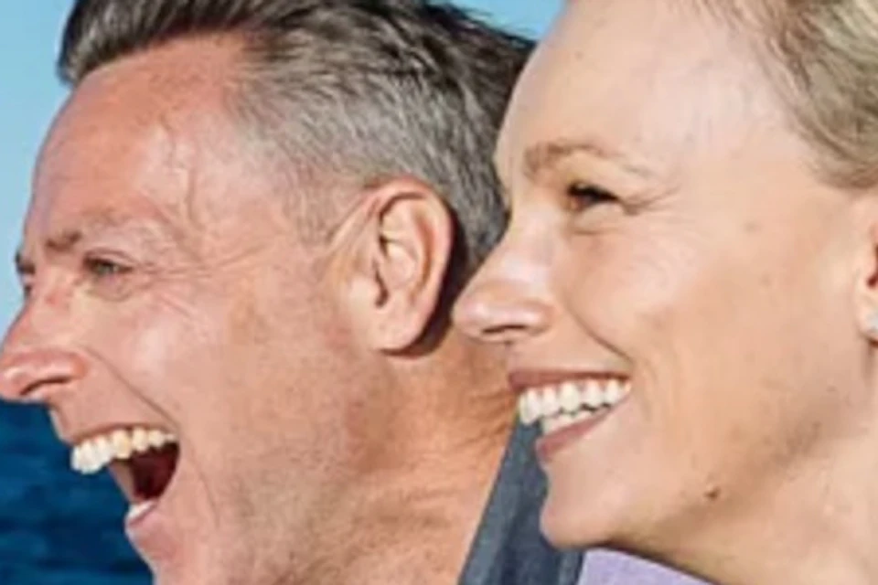 A man and a woman on a boat smiling and pointing towards the ocean under a clear sky.