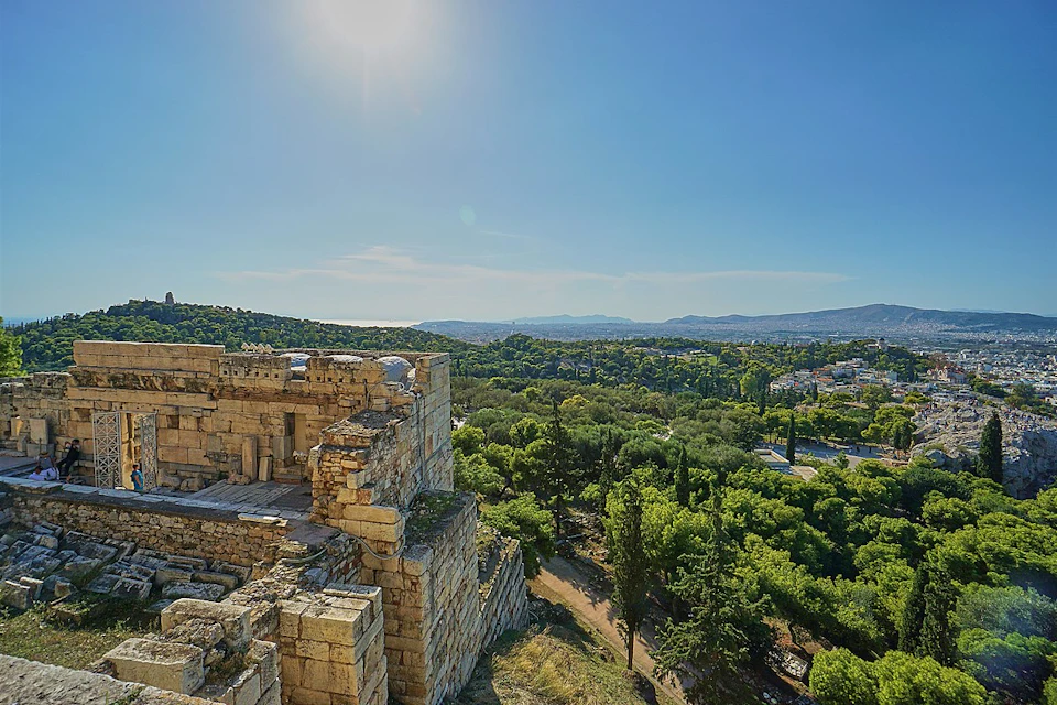 Ancient stone structure with a sprawling green forest and distant mountains under a bright, clear sky.