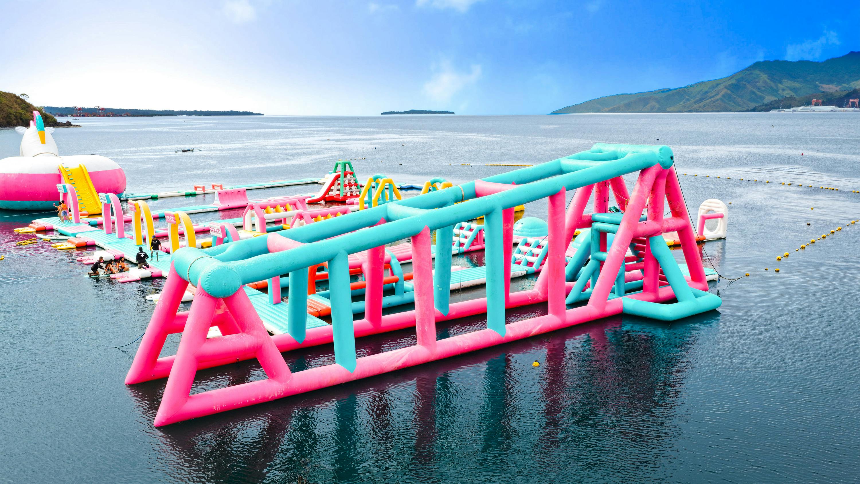 A colorful inflatable water park with slides and obstacles floating on a calm sea under a blue sky.