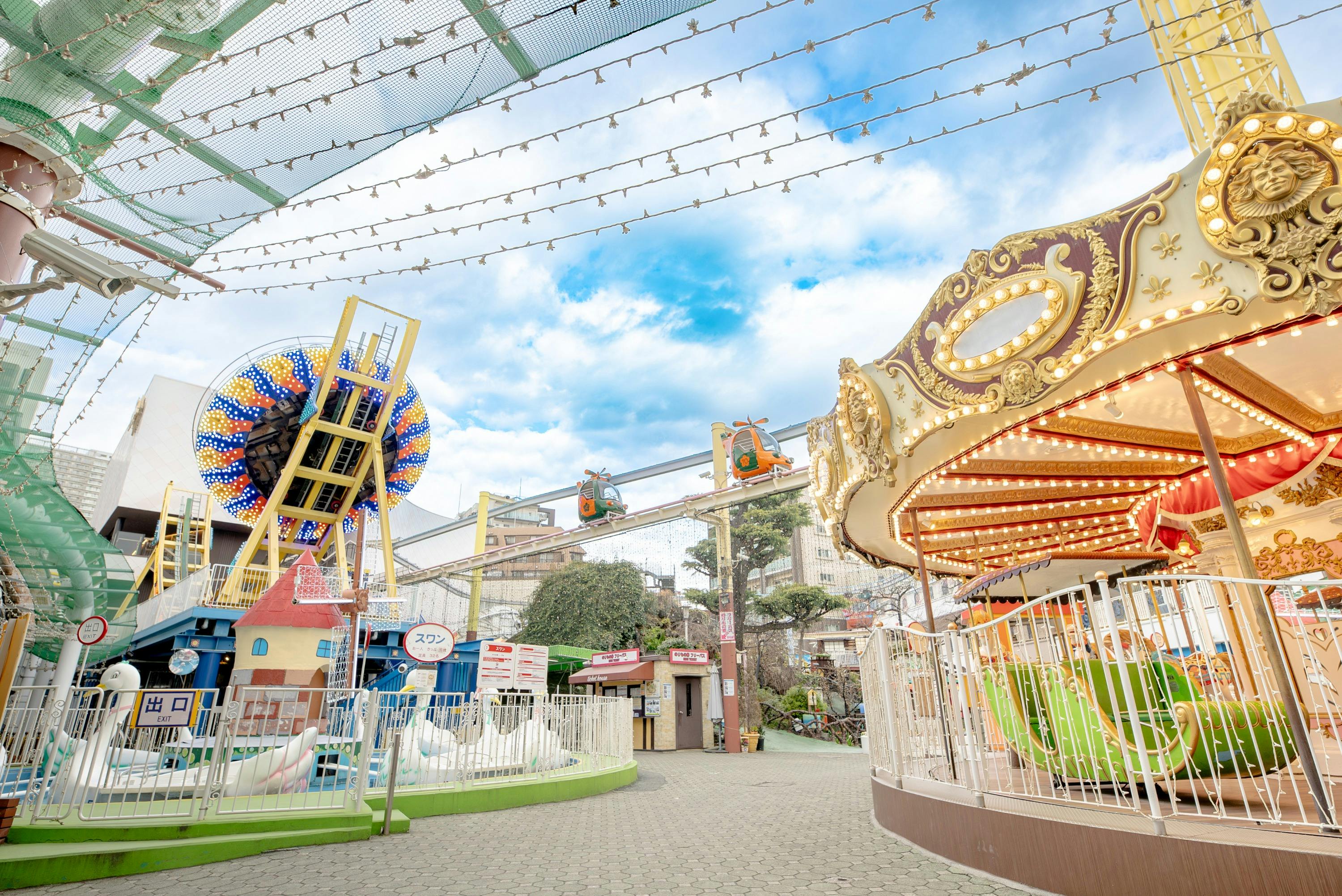 An amusement park with a carousel, a Ferris wheel, and rides under string lights and a cloudy blue sky.