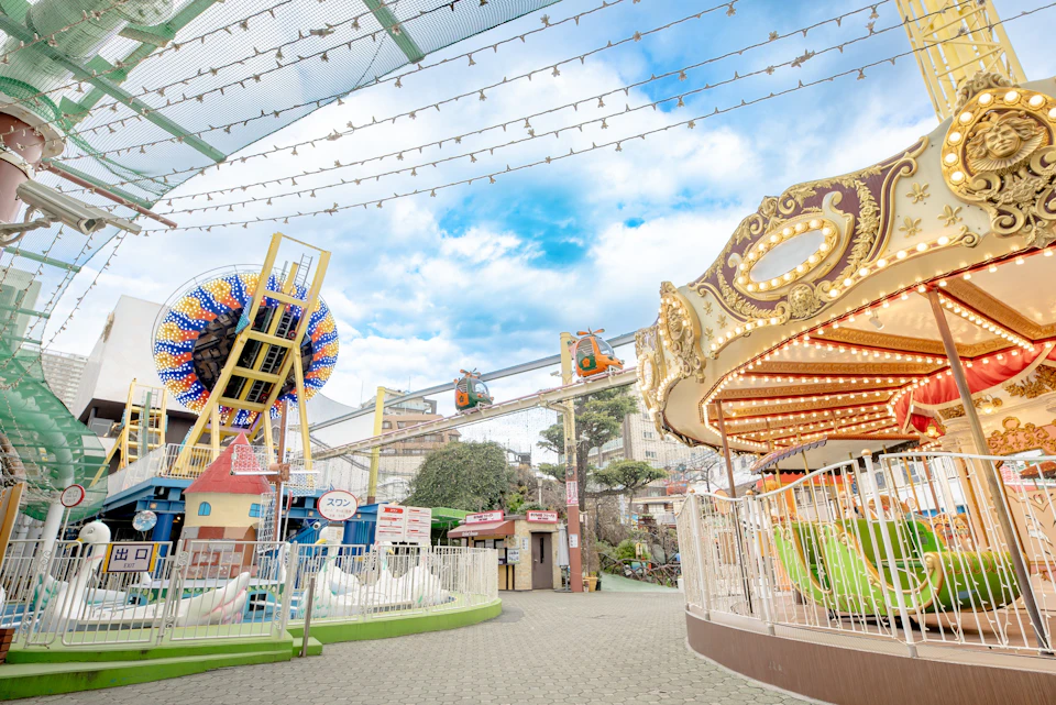 An amusement park with a carousel, a Ferris wheel, and rides under string lights and a cloudy blue sky.