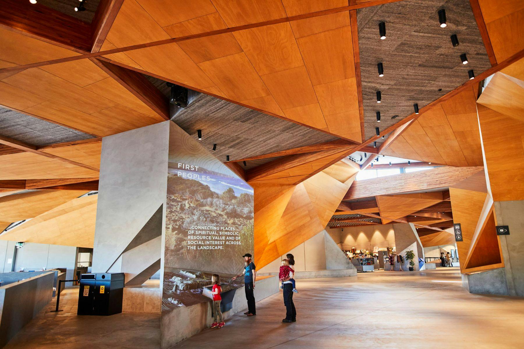 三人入住一栋配有几何形木质天花板的现代化建筑。 一个人阅读有关第一民族的墙面展示。