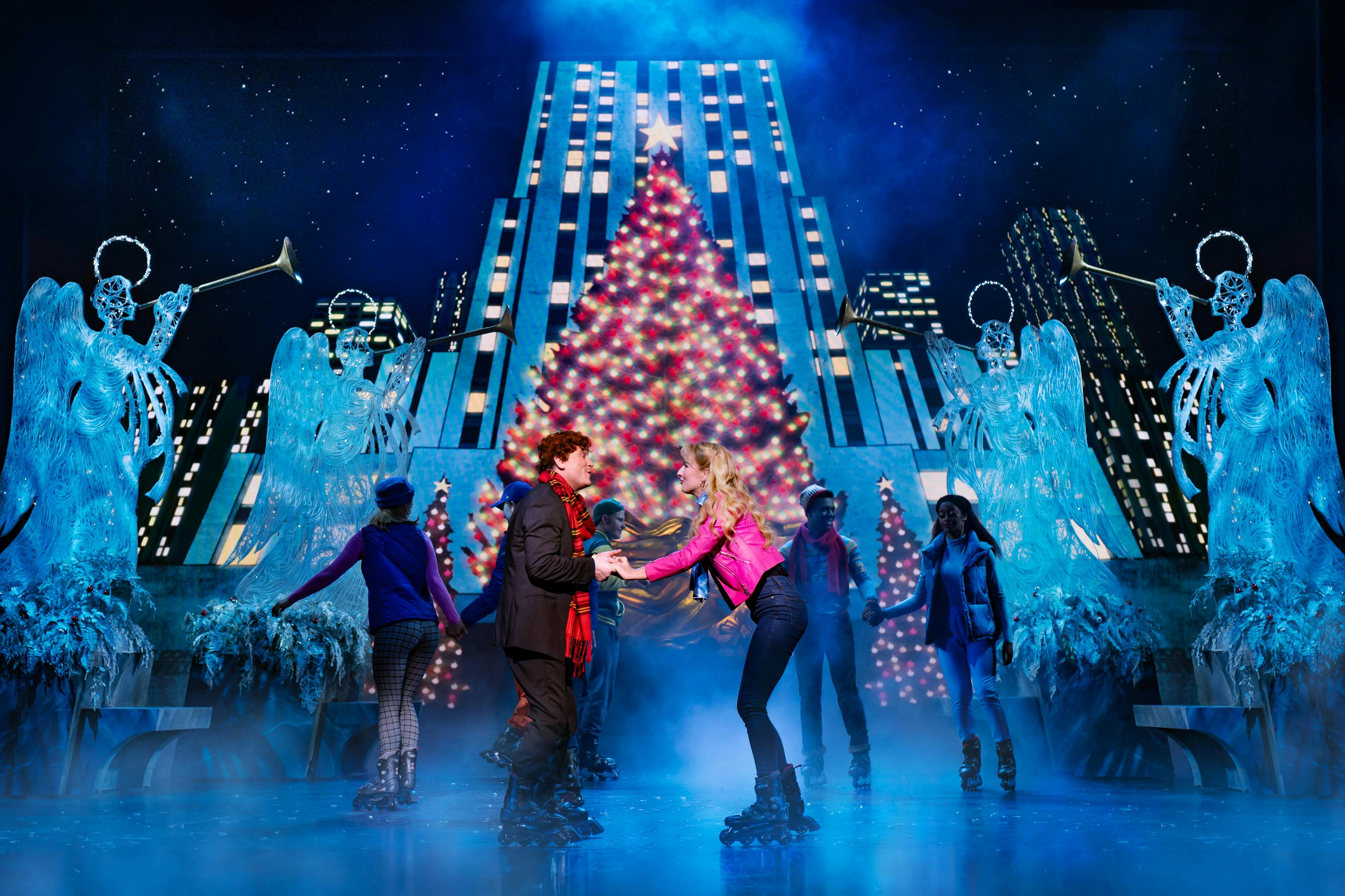People ice skating in front of a large, decorated Christmas tree with a star on top, surrounded by festive lights and statues.