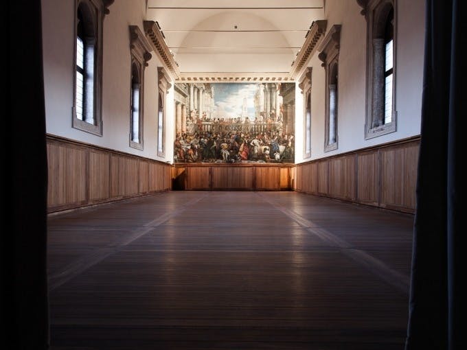 Большая пустая комната с деревянными полами и стеновыми панелями с подробной настенной росписью на дальней стене.