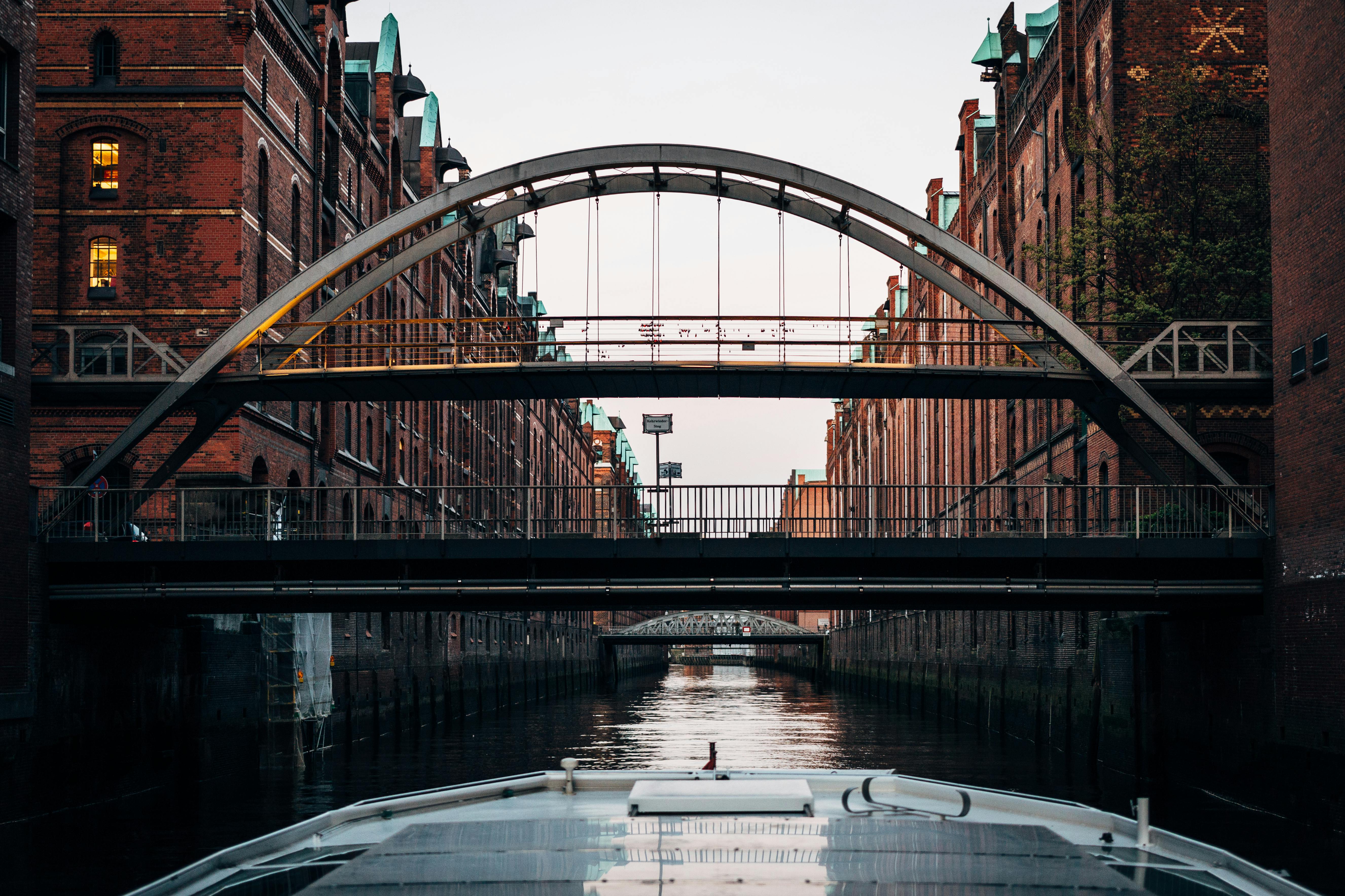 Murstensbygninger ligger langs en kanal med flere broer over hovedet, set fra en båd.