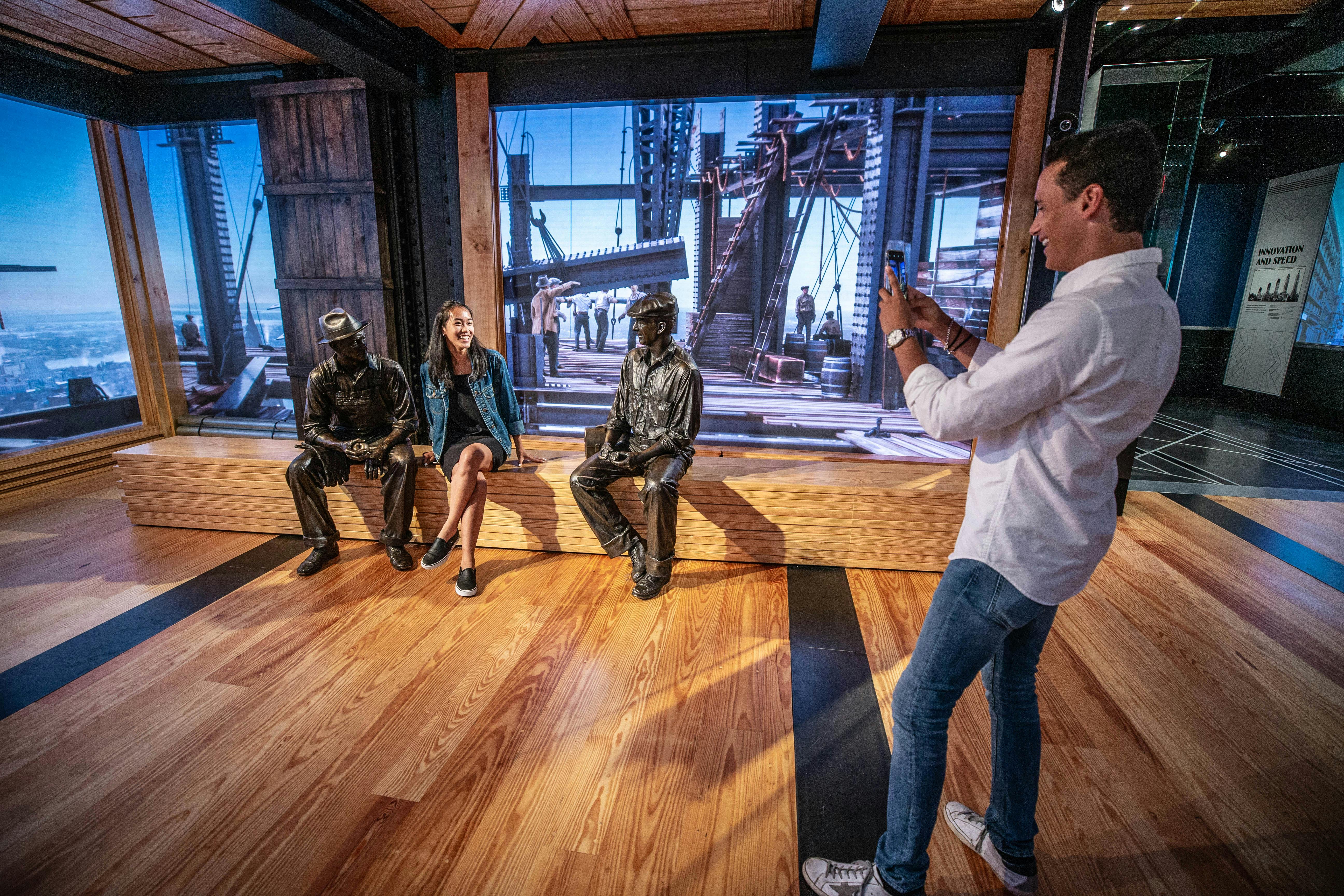 Un uomo fotografa una donna seduta e una statua di bronzo in un museo con pavimenti in legno e una mostra a tema industriale.