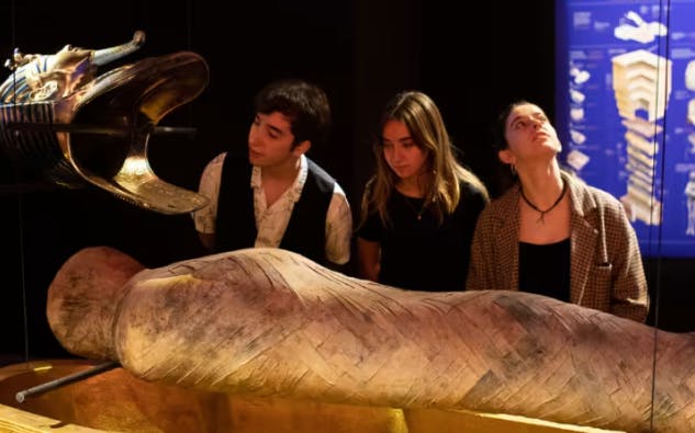 Tres personas observan una exposición de momias en un museo poco iluminado.