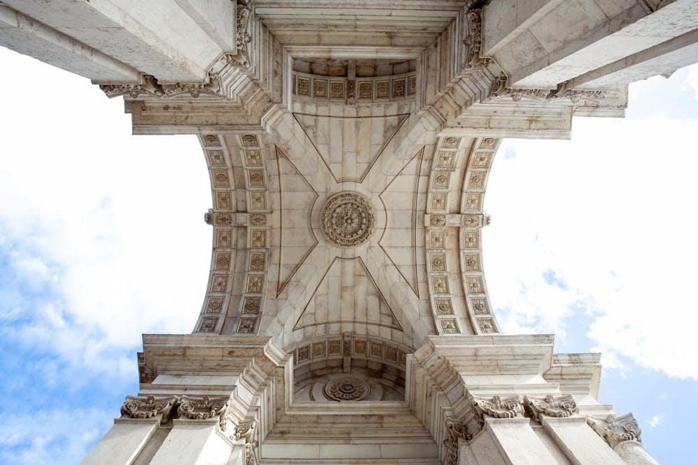 抬头看着拱门的华丽石头天花板，上面有错综复杂的雕刻和建筑细节，与部分多云的天空相映成趣。