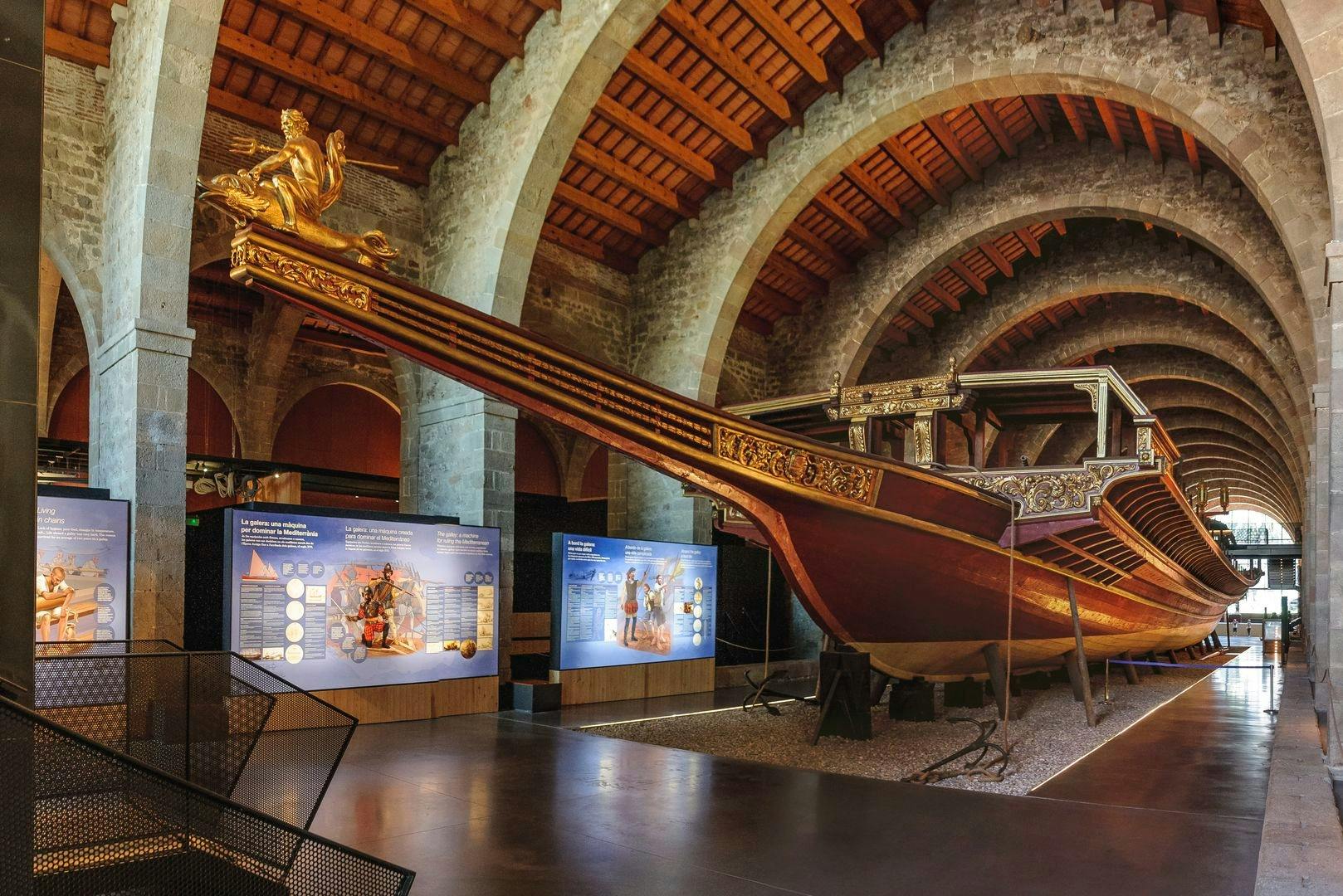 A large, ornate wooden ship inside a stone-arched museum exhibit, with educational display boards nearby.