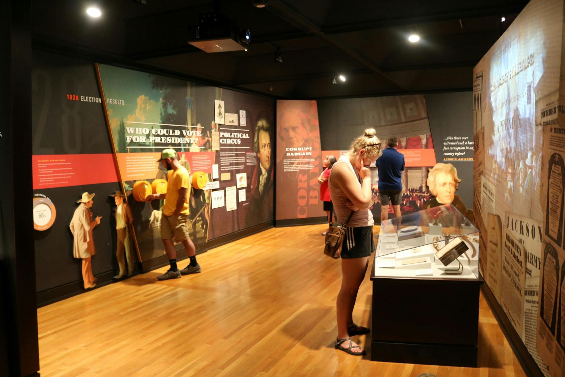 Visitors explore a museum exhibit featuring historical displays, photos, and artifacts on walls and in a glass case.
