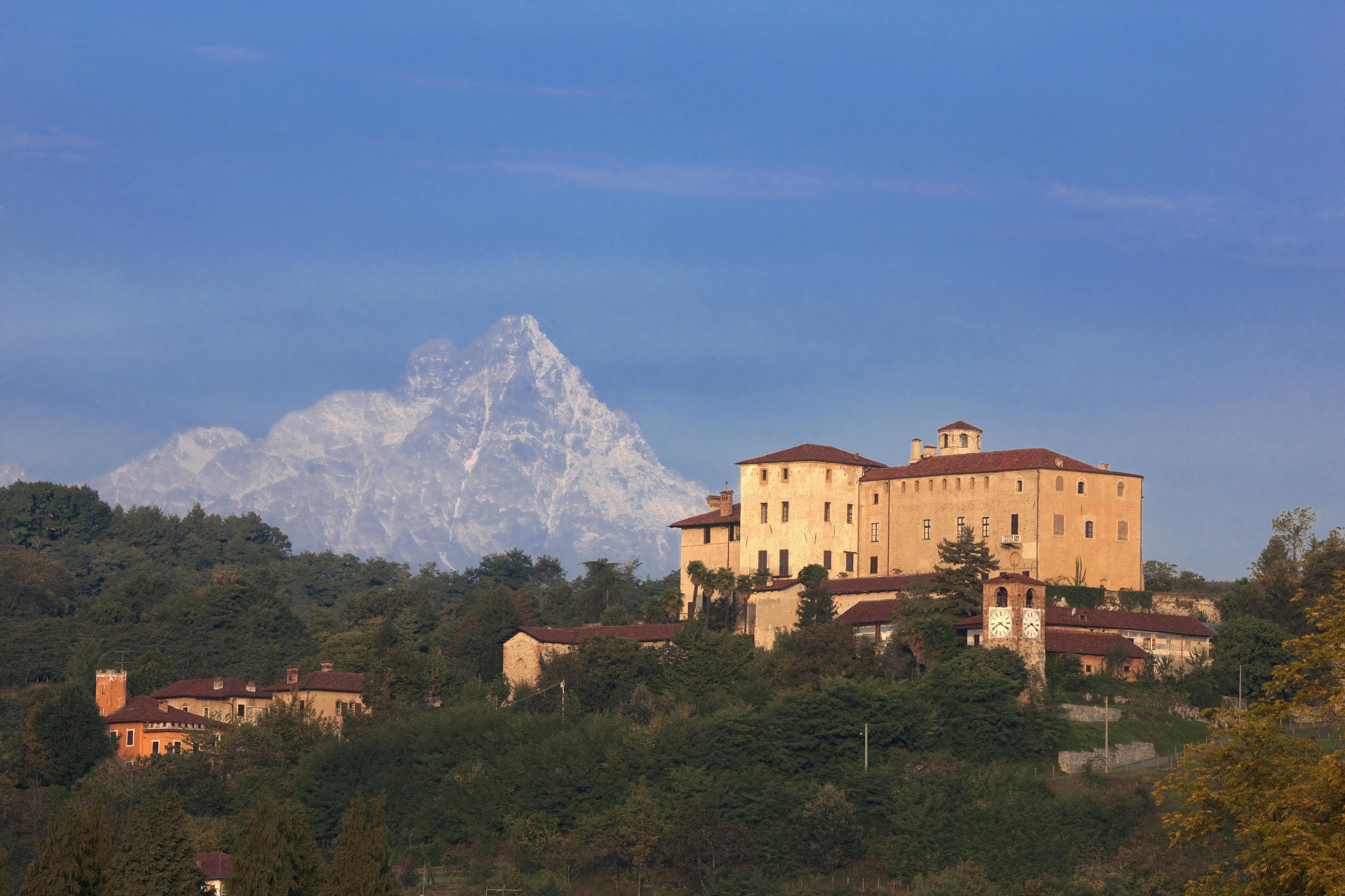 这座历史悠久的建筑位于一座小山上，前景是一片森林，背景是晴朗的天空下白雪皑皑的山脉。