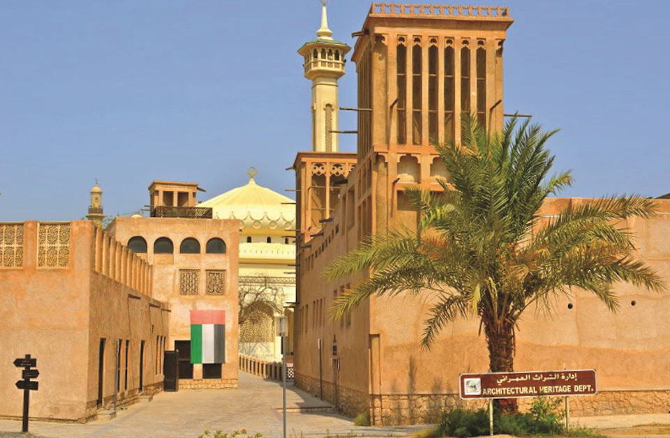 Traditional Middle Eastern buildings with wind towers, a palm tree, and a sign reading "Architectural Heritage." A mosque is in the background.