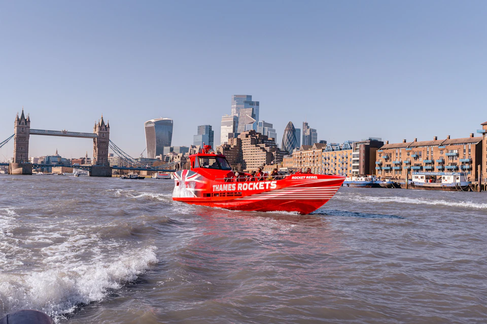 A red speedboat labeled "Thames Rockets" travels on the River Thames in London, with city landmarks in the background.