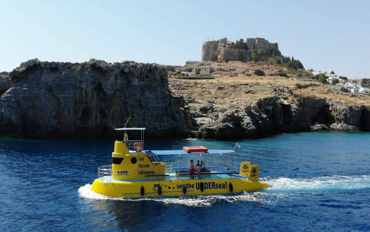 A yellow submarine-like boat on blue water with cliffs and an ancient castle in the background.