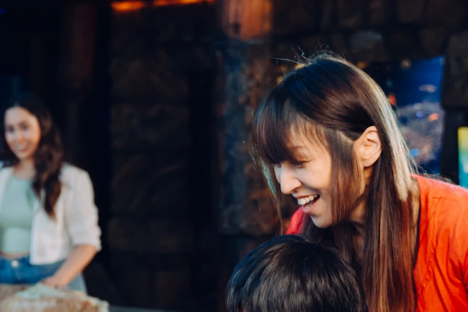 A woman in a blue uniform interacts with visitors at a touch tank in an aquarium with rocks and a mural background.